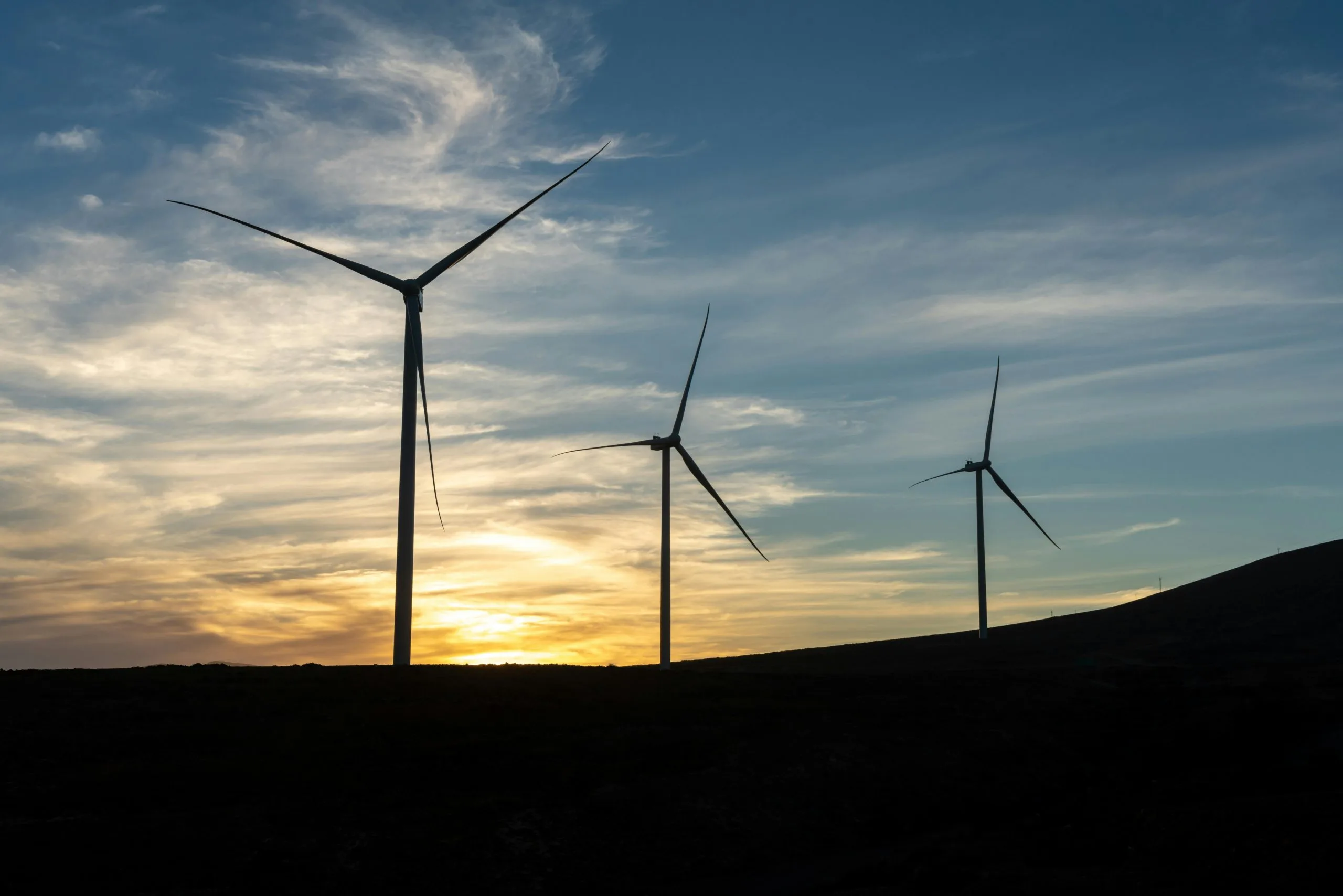 Three wind turbines captured during sunset sky with scattered clouds.